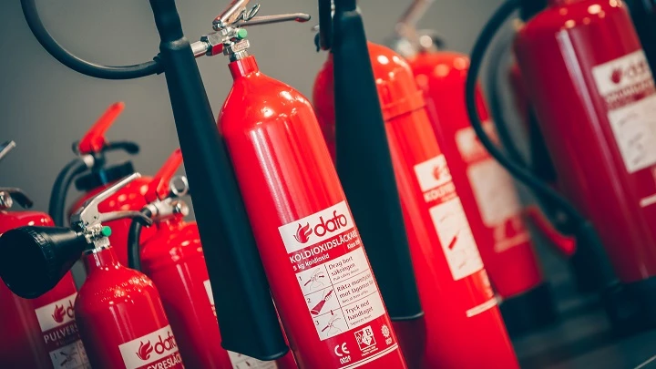 Flera röda släckare tillsammans Flera röda koldioxidsläckare står tillsammans mot mörk bakgrund. Släckarna har vit text och svart munstycke.